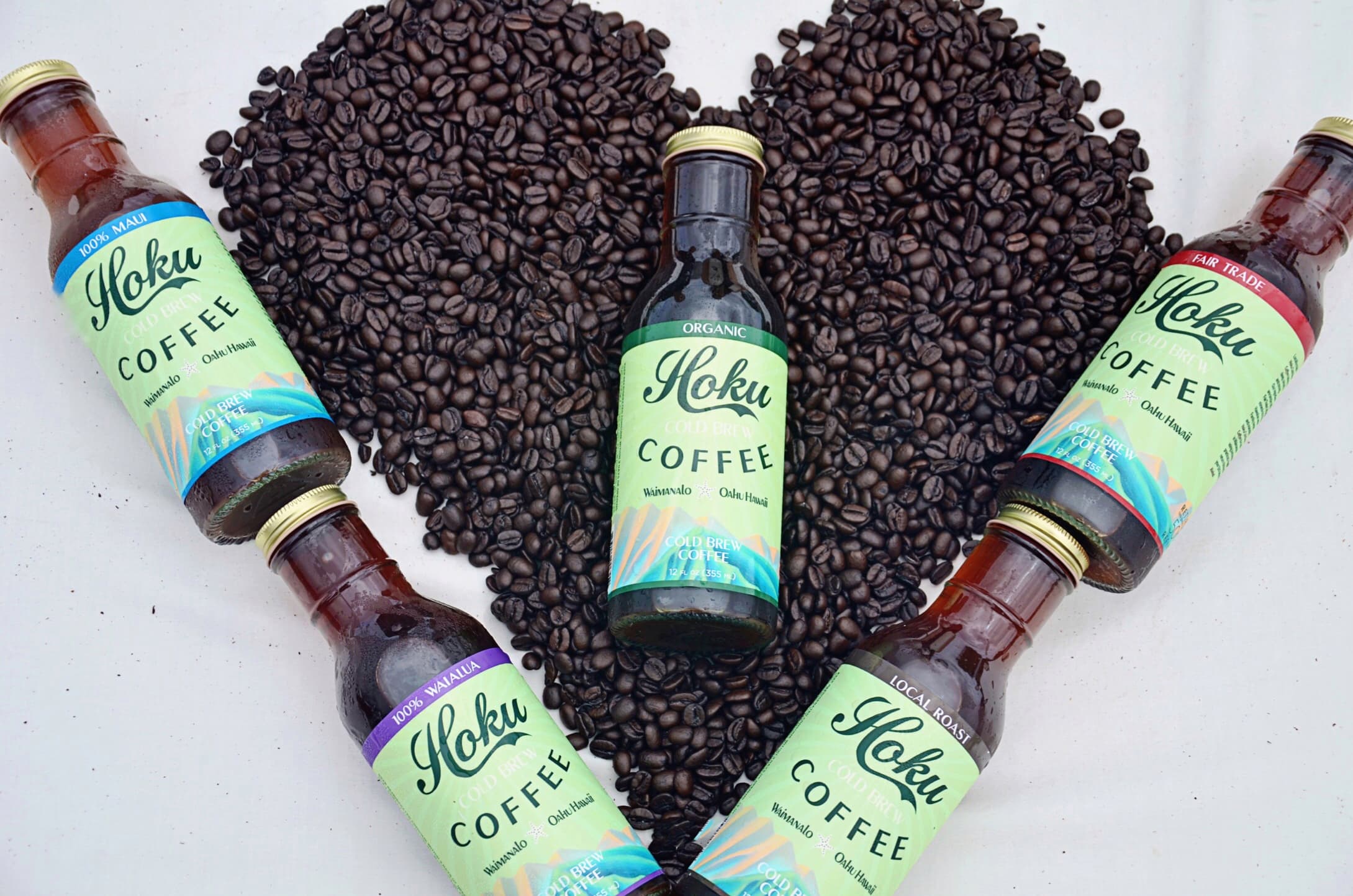 Five Hoku Cold Brew bottles arranged around a heart of coffee beans