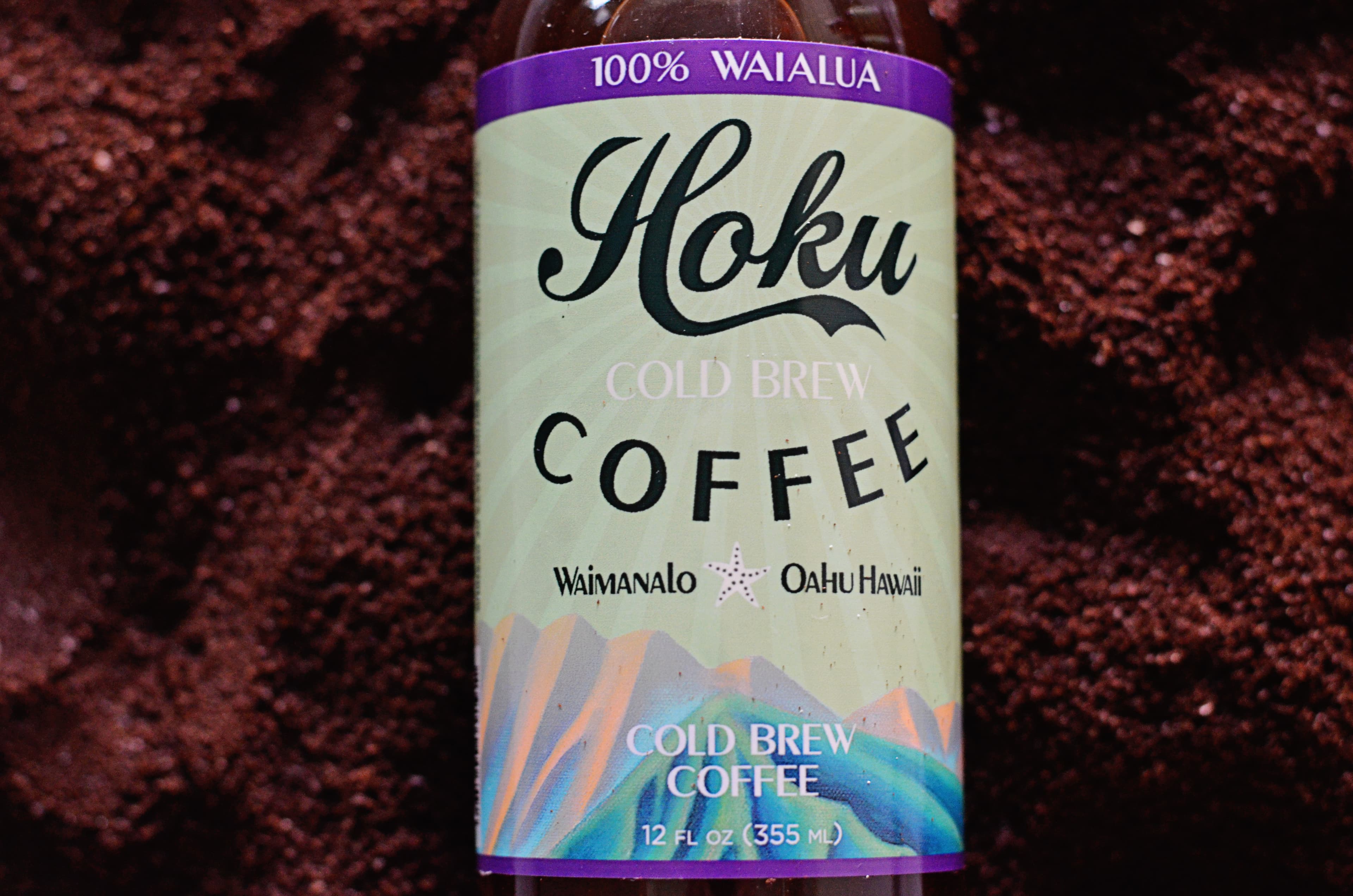 Hoku 100% Waialua cold brew bottle resting on coffee grounds